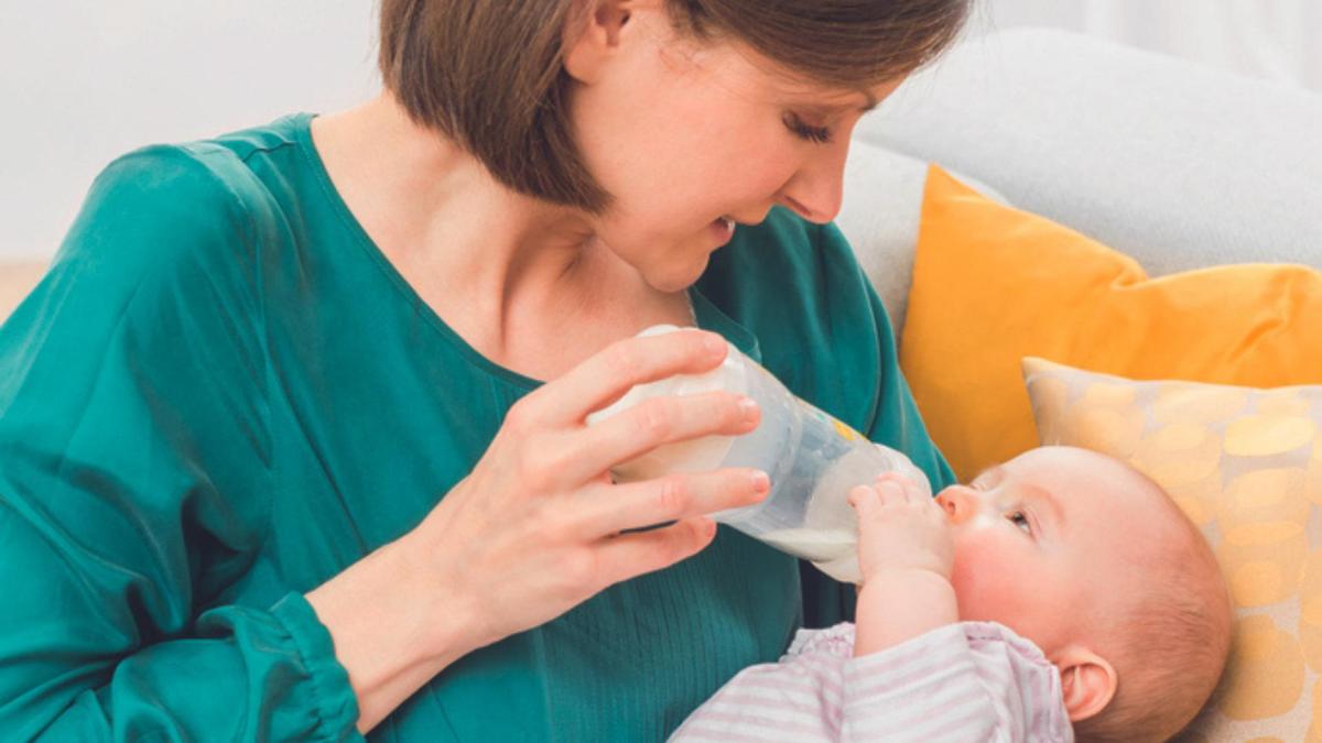 Maminka krmí lahvičkou miminko, kojenec drží lahvičku jednou rukou