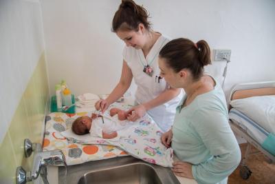 Porodnice Mulačova. Mulačova nemocnice, s.r.o., Gynekologicko-porodnické oddělení: Sestřička pomáhající mamince s novorozeným miminkem.