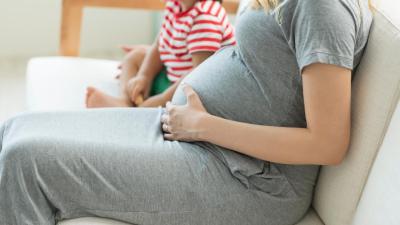 Těhotná žena s dítětem sedí na gauči. Preeklampsie u druhého těhotenství.