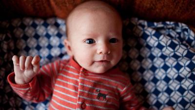 Malé miminko leží v posteli a usmívá se, homeopatie u novorozenců
