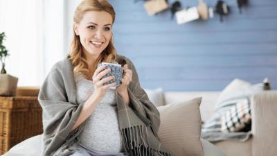 Těhotná žena pije doma čaj zabalená do deky