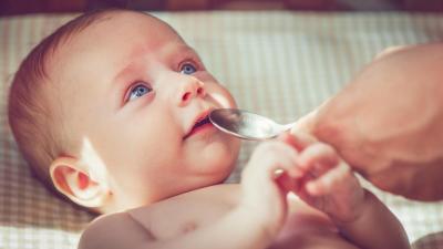 Rodič podává malému dítěti vodu s homeopatickým přípravkem na lžičce