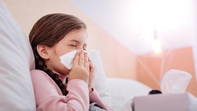 Alergické dítě kýchá do kapesníku v posteli.