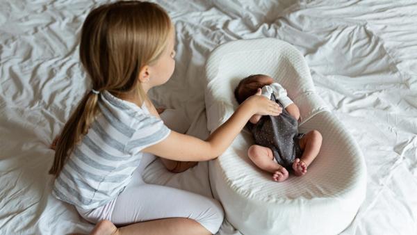 Sestřička hladí malého sourozence v hnízdečku.