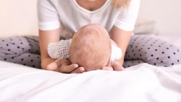 Maminka sedí v tureckém sedu s miminkem na posteli. Obnova pánevního dna po porodu s Aniballem.