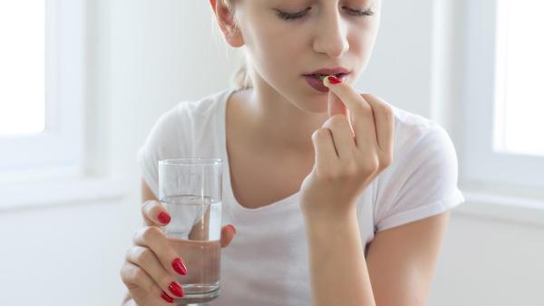 Žena se chystá spolknout vitamín na podporu růstu vlasů.