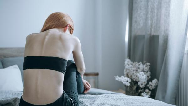 Hubená žena sedí sklíčeně v posteli, poruchy příjmu potravy