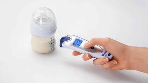 ruka, která drží teploměr Veroval Baby a měří s ním teplotu mléka v dětské lahvičce