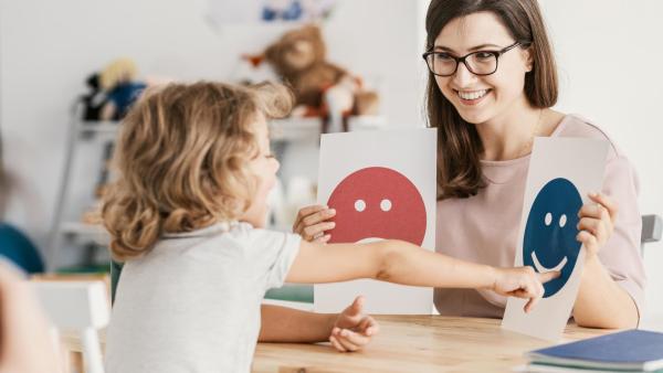 Odborník se věnuje dítěti s atypickým autismem. Dítě ukazuje na smějícího se smajlíka.