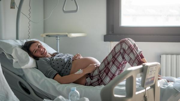 Těhotná žena si drží bříško na nemocničním lůžku, císařský řez na přání