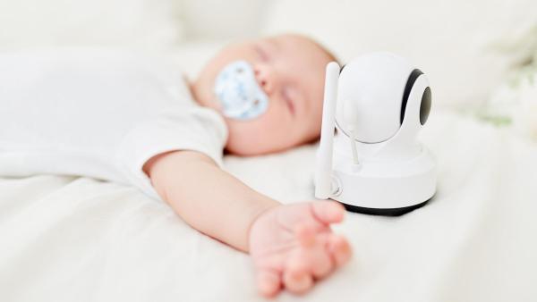 Spící dítě s dudlíkem v postýlce, v popředí monitor dechu nebo chůvička.