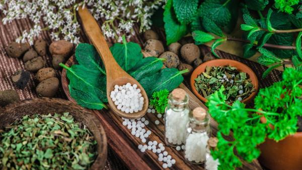 homeopatické léky na lžičce a mísy plné bylinek