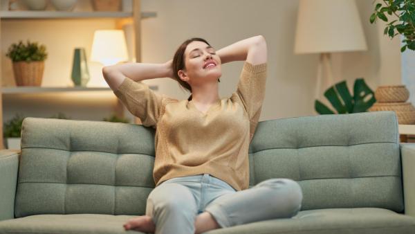 Spokojená žena sedící na gauči relaxuje. Emoční rovnováha a klid.