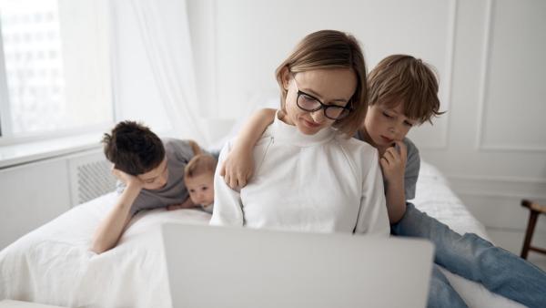 Maminka se třemi dětmi sedí na posteli a pracuje.