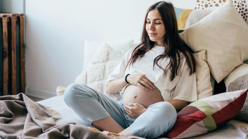 Těhotná žena sedí v posteli a drží si těhotenské bříško