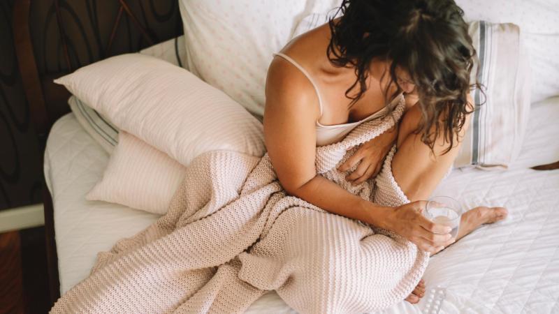 Žena sedí v posteli a drží si bolavé břicho, endometrióza.