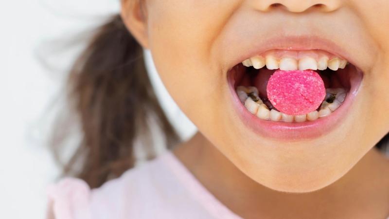 Holčička se zkaženými zuby drží sladký bonbon v puse