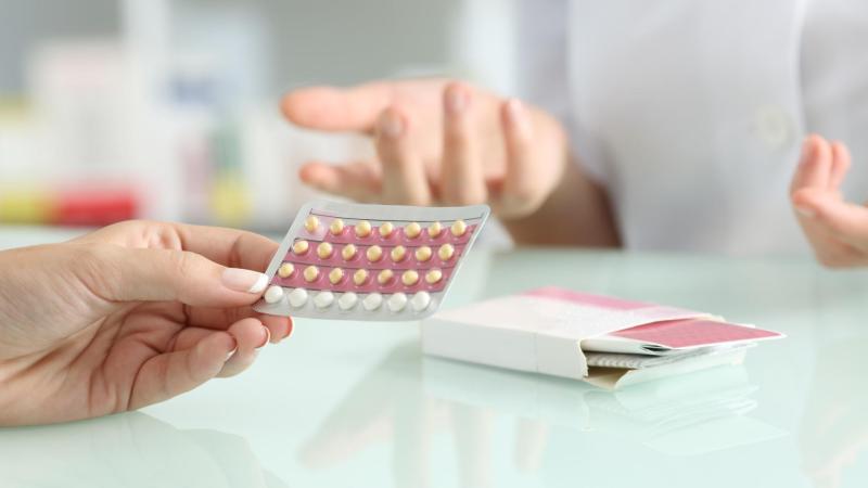 Žena drží v ruce hormonální antikoncepce a konzultuje s lékařem.