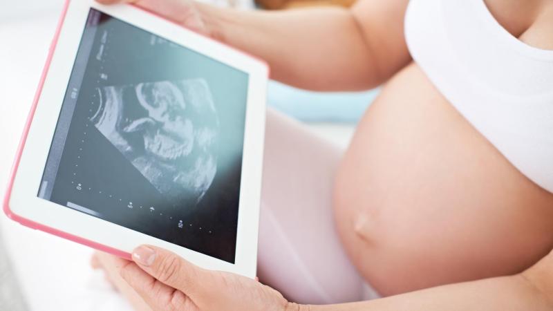 Těhotná žena drží tablet se snímkem z ultrazvuku.