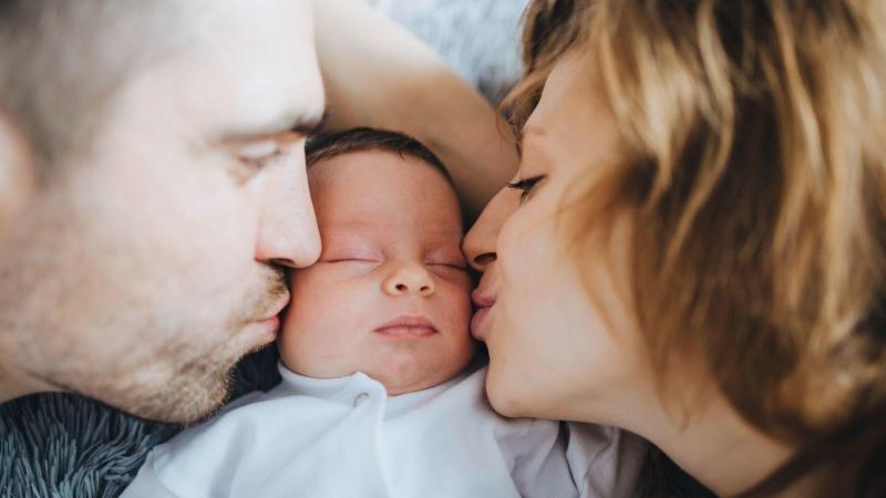 Rodiče líbají spícího novorozence na tvář, spánek novorozenců.