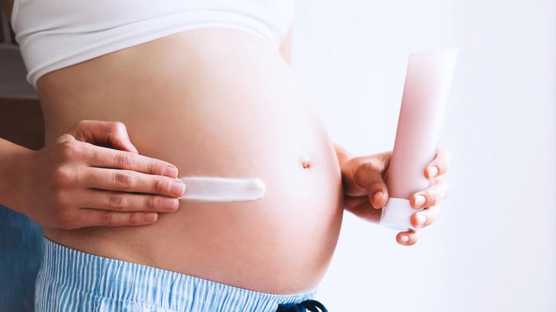 Žena si maže krém na strie na těhotenské bříško, strie v těhotenství
