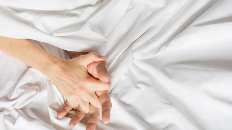 Muž a žena se drží za ruce v posteli
