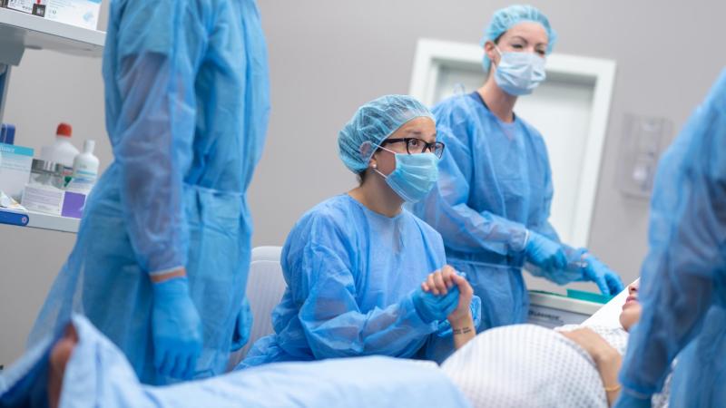Těhotná maminka na operačním sále drží doktorku za ruku a čeká na císařský řez.