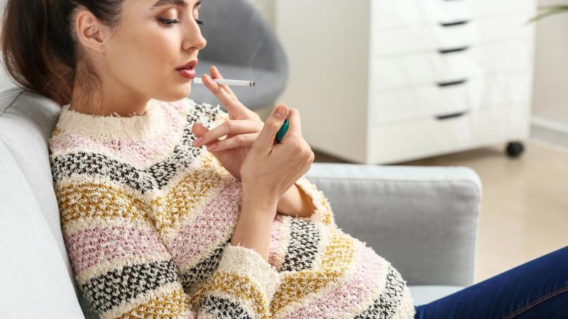 Těhotná žena na gauči si zapaluje cigaretu.
