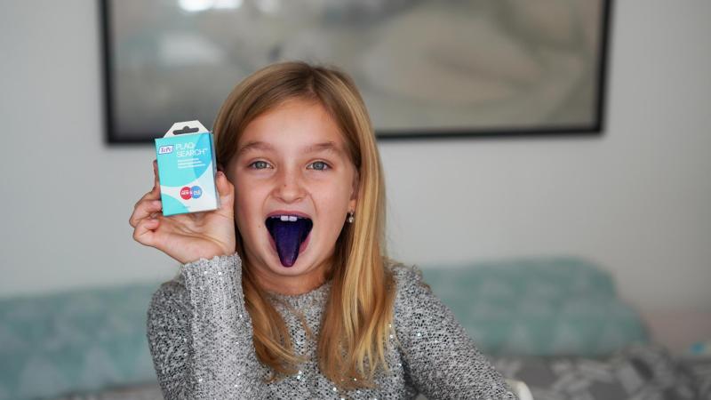 Holčička ukazuje modře zbarvený jazyk po tabletkách na zubní plak