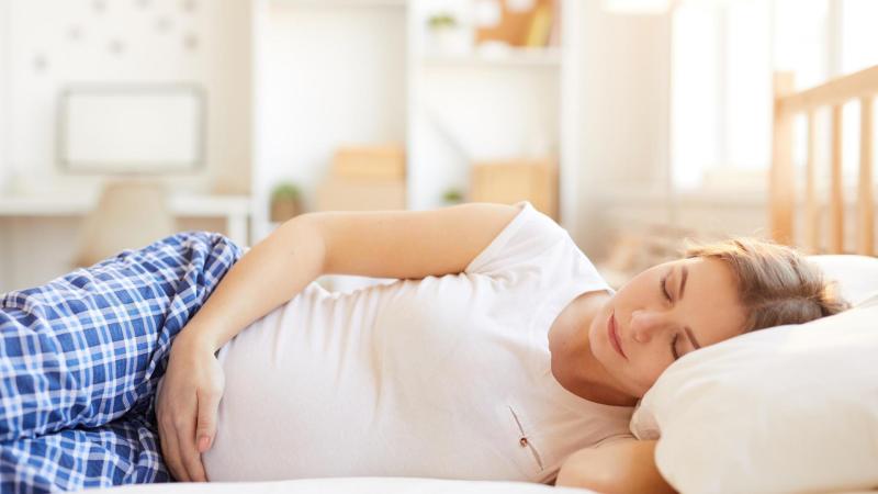Těhotná žena spí v posteli. Rizikové těhotenství a ambulantní porod.