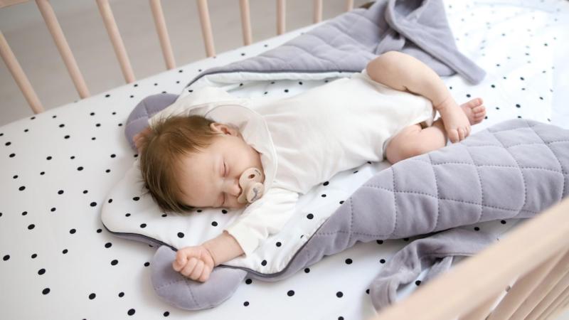 Miminko spí ve své postýlce a zavinovačce, spánek novorozence.
