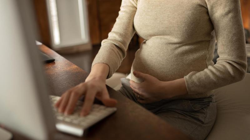 Těhotná žena sedí na gauči a vyhledává informace o ambulantním porodu na počítači.