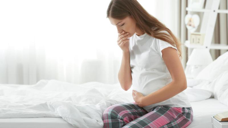 Těhotná žena na posteli má nevolnosti.