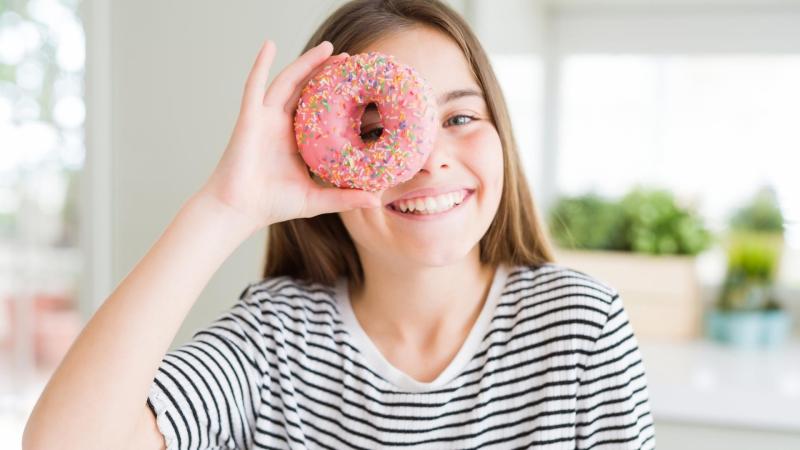 Dívka ukazuje donut s růžovou polevou
