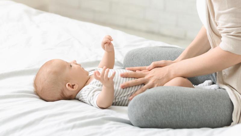 Maminka na posteli masíruje bříško miminka, dětská kolika