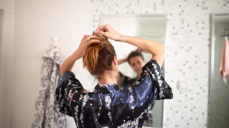 Žena si dělá v koupelně culík před zrcadlem