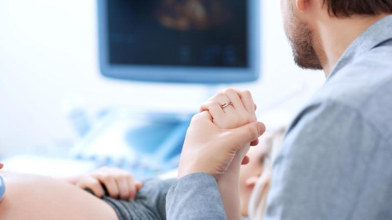 Partner drží za ruku ženu, která absolvuje screening v 1. trimestru.