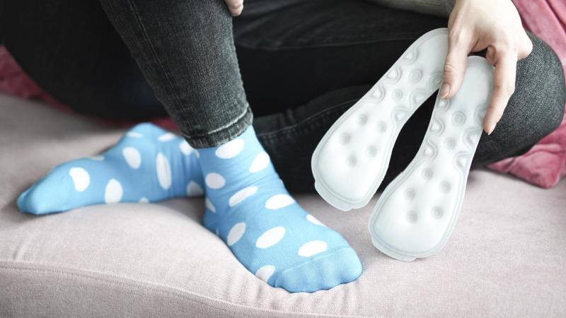 Dívka sedí na gouči, má na sobě modré puntíkaté ponožky eMimino a v ruce drží vložky do bot MEDICOVI.