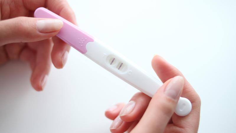 Žena drží pozitivní těhotenský test.