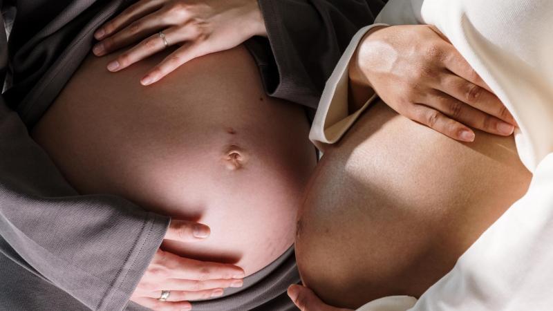 Dvě těhotné ženy stojí naproti sobě a drží se za břicho, velikost bříška