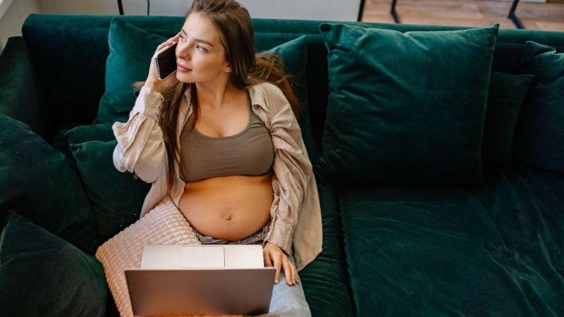 Těhotná žena telefonuje a čte informace na notebooku
