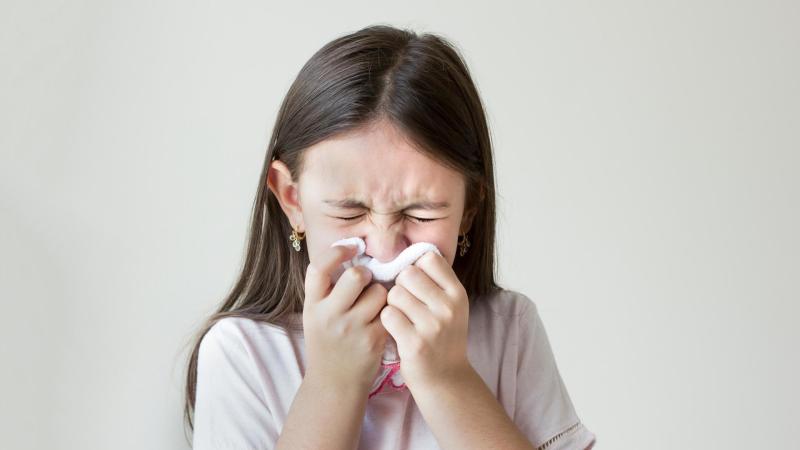 Alergické dítě kýchá do kapesníku.