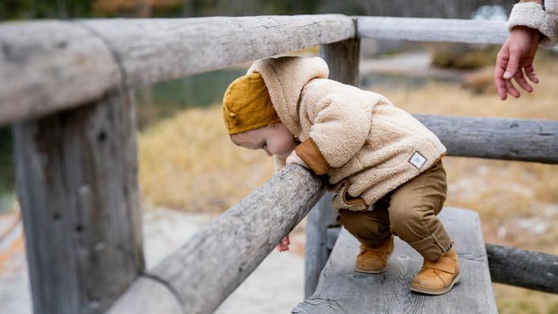 Malé dítě si hraje na dřevěné lavičce oblečené v teplé bundě a mikině