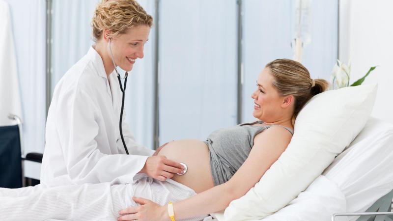 Doktorka poslouchá miminko těhotné ženy přes břicho. Ambulantní porod.