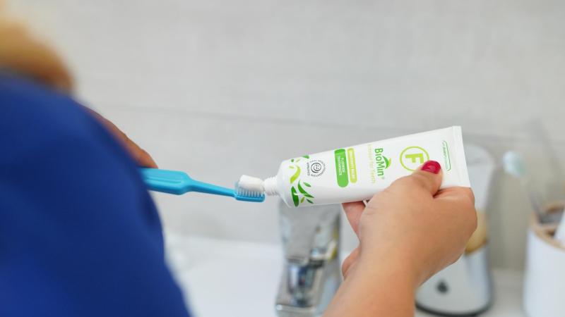 Žena si na kartáček TePe nanáší zubní pastu s fluoridem, čištění zubů v těhotenství.