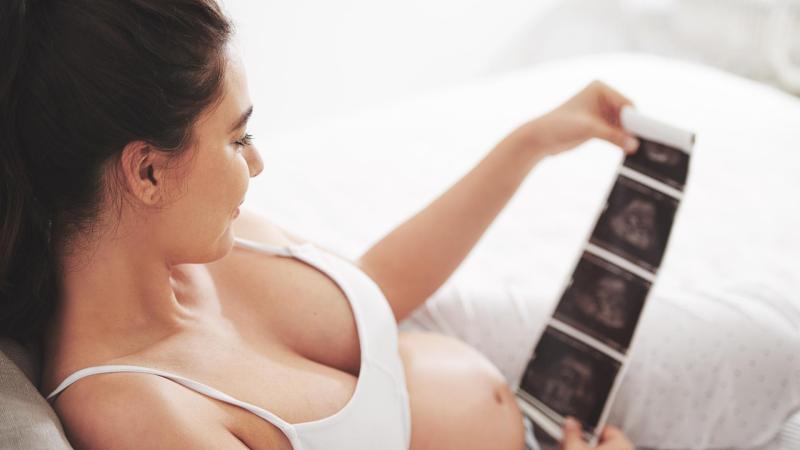 Těhotná žena se kouká na fotky ultrazvuku miminka v bříšku.