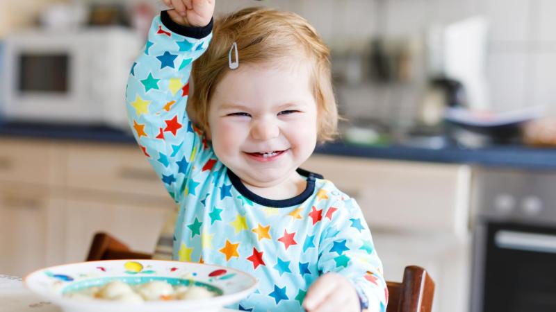 Smějící se dítě v kuchyni má před sebou talíř s jídlem. Zdravá strava.