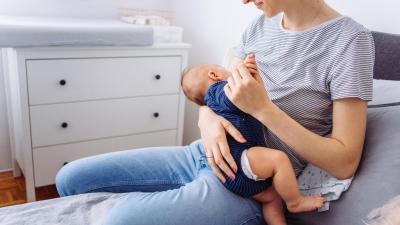 Maminka sedí na posteli a kojí miminko. Psychosociální efekt kojení.