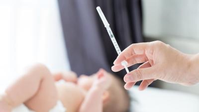Lékař drží v ruce injekci. V pozadí leží dítě. Povinné očkování.
