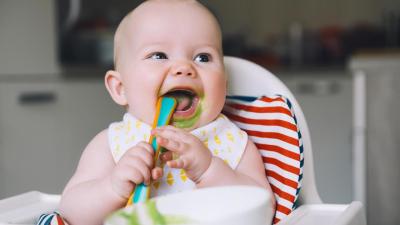 Krmení miminka a společné stolování. Miminko sedí na židličce a papá zeleninovou kaší.